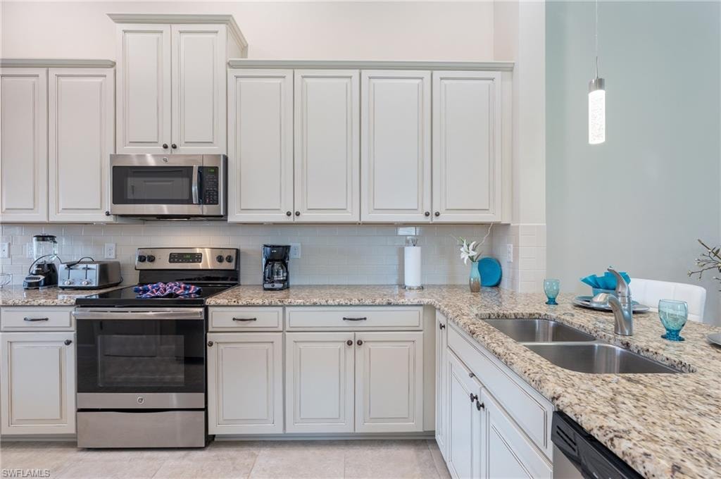 Kitchen with stainless steel appliances, light stone countertops, decorative backsplash, and white cabinetry