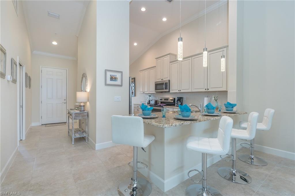 Kitchen with crown molding, a kitchen bar, decorative light fixtures, light stone countertops, and a peninsula