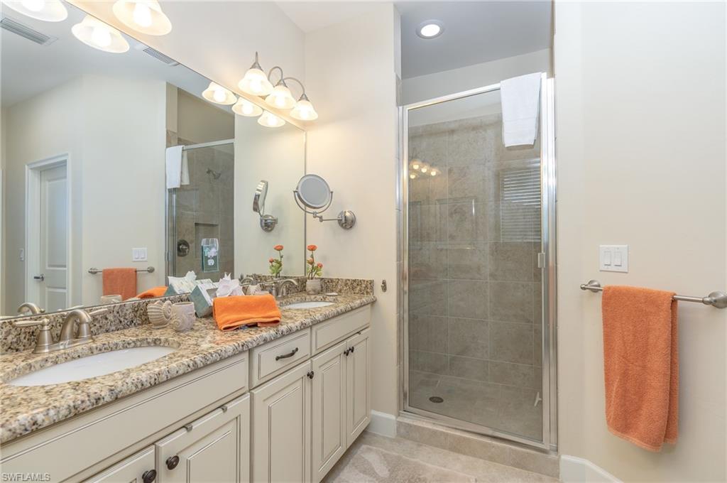 Full bath with a shower stall, double vanity, and light tile patterned flooring