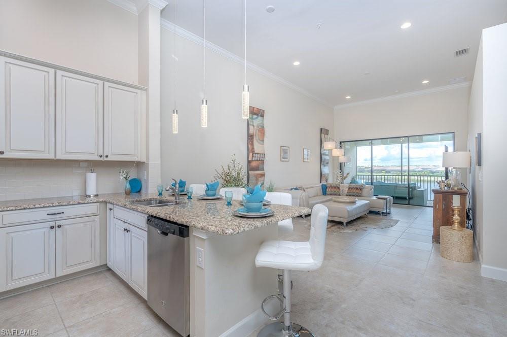 Kitchen featuring backsplash, light stone counters, crown molding, a kitchen bar, and pendant lighting