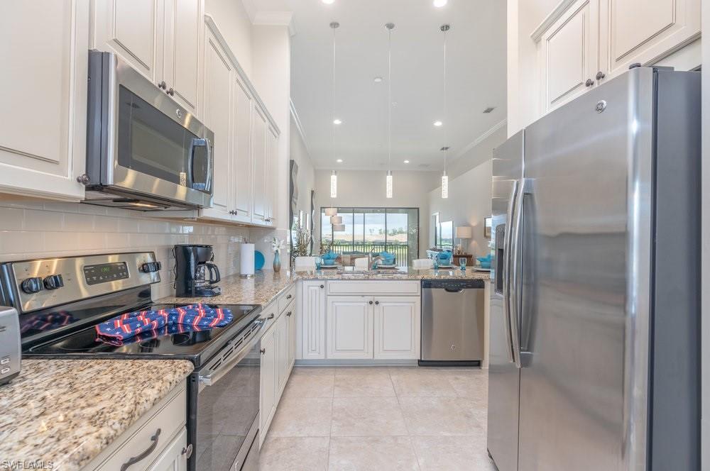 Kitchen with stainless steel appliances, light stone counters, hanging light fixtures, backsplash, and white cabinets