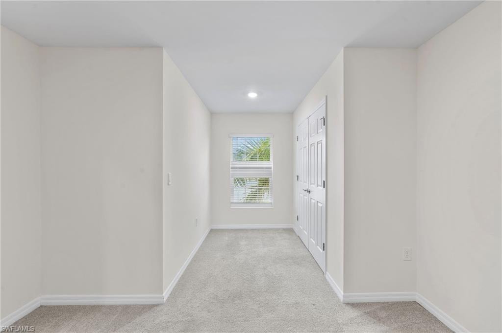 Hallway with light colored carpet and baseboards