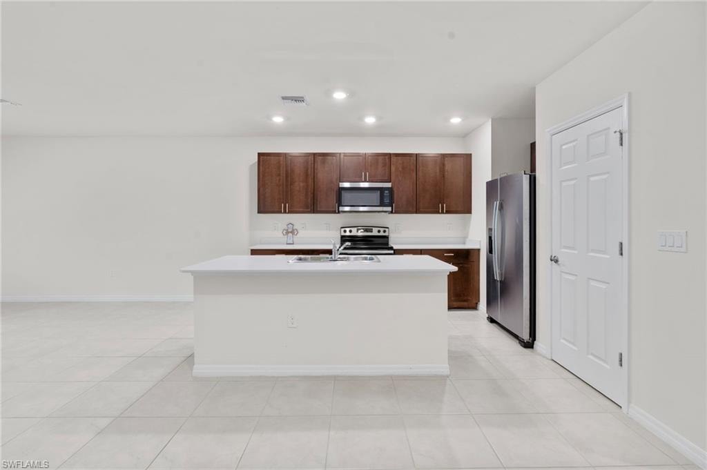 Kitchen featuring stainless steel appliances, a kitchen island with sink, dark brown cabinets, light tile patterned floors, and recessed lighting