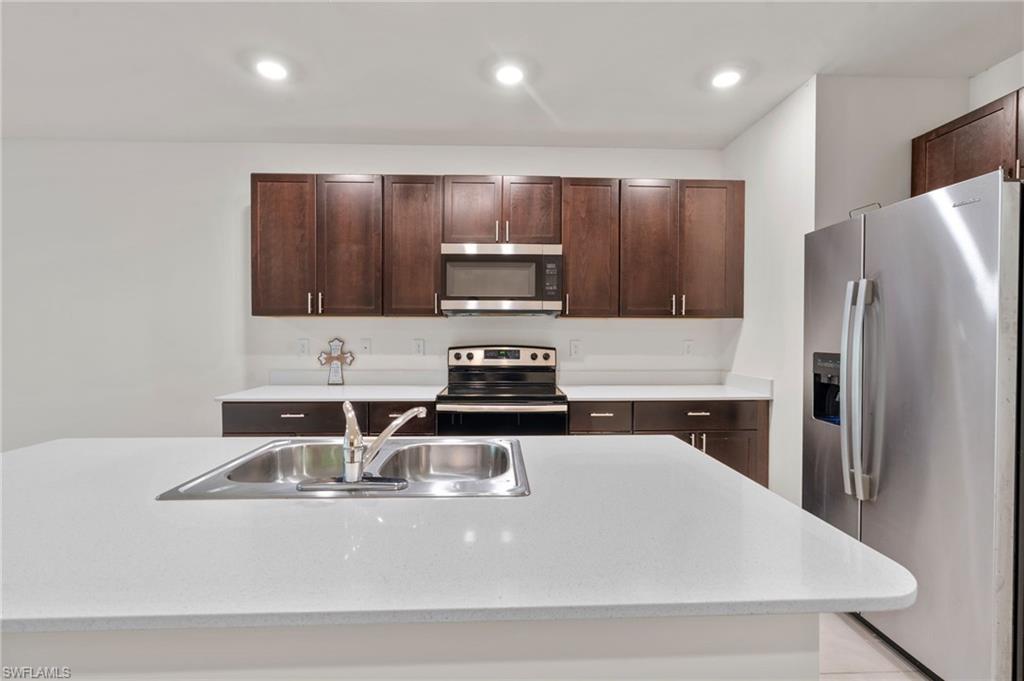 Kitchen with appliances with stainless steel finishes, dark brown cabinetry, light stone counters, and recessed lighting