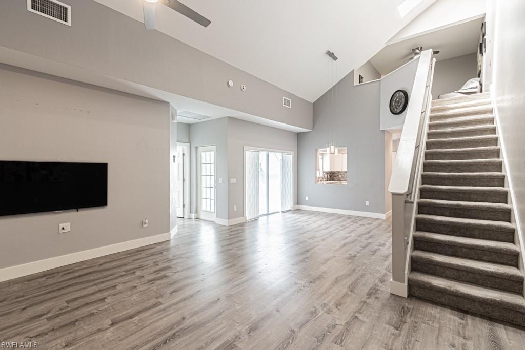 Unfurnished living room with light wood-style flooring, stairs, high vaulted ceiling, and a ceiling fan