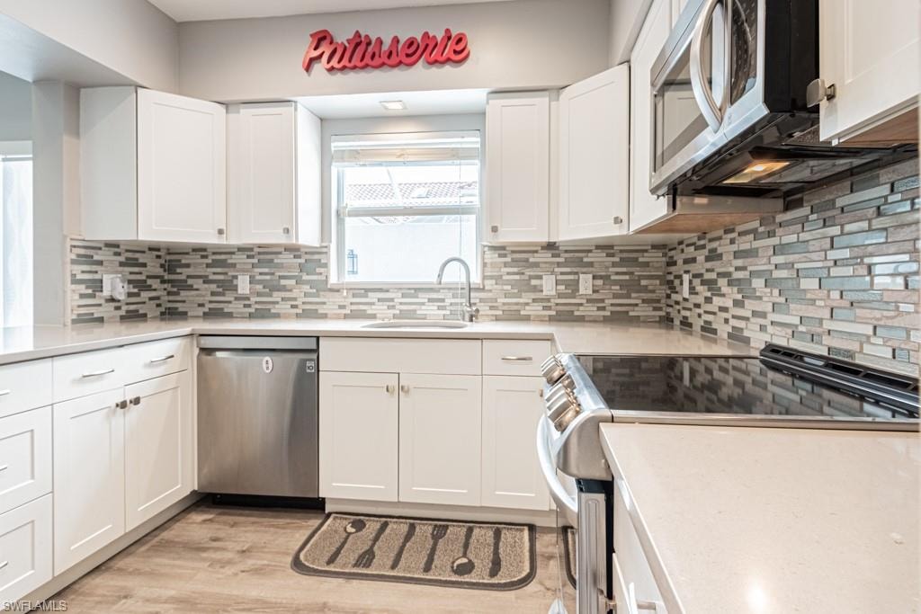 Kitchen featuring appliances with stainless steel finishes, white cabinets, light wood-style floors, and light stone countertops