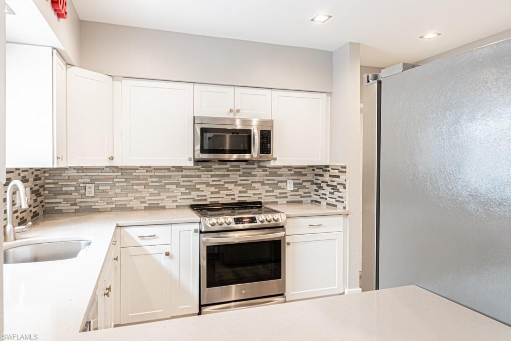 Kitchen with appliances with stainless steel finishes, white cabinetry, light stone countertops, backsplash, and recessed lighting