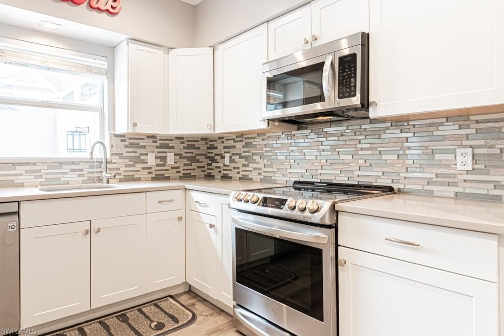 Kitchen with stainless steel appliances, white cabinetry, light wood finished floors, backsplash, and light stone counters
