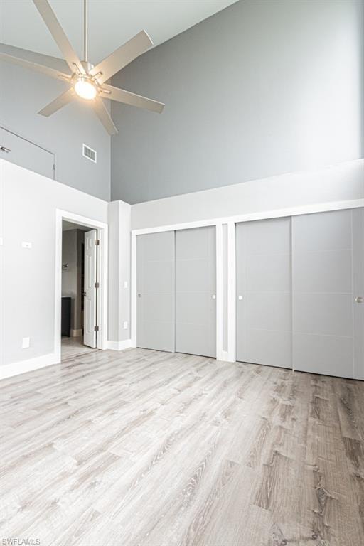 Unfurnished bedroom featuring high vaulted ceiling, two closets, light wood-type flooring, and ceiling fan