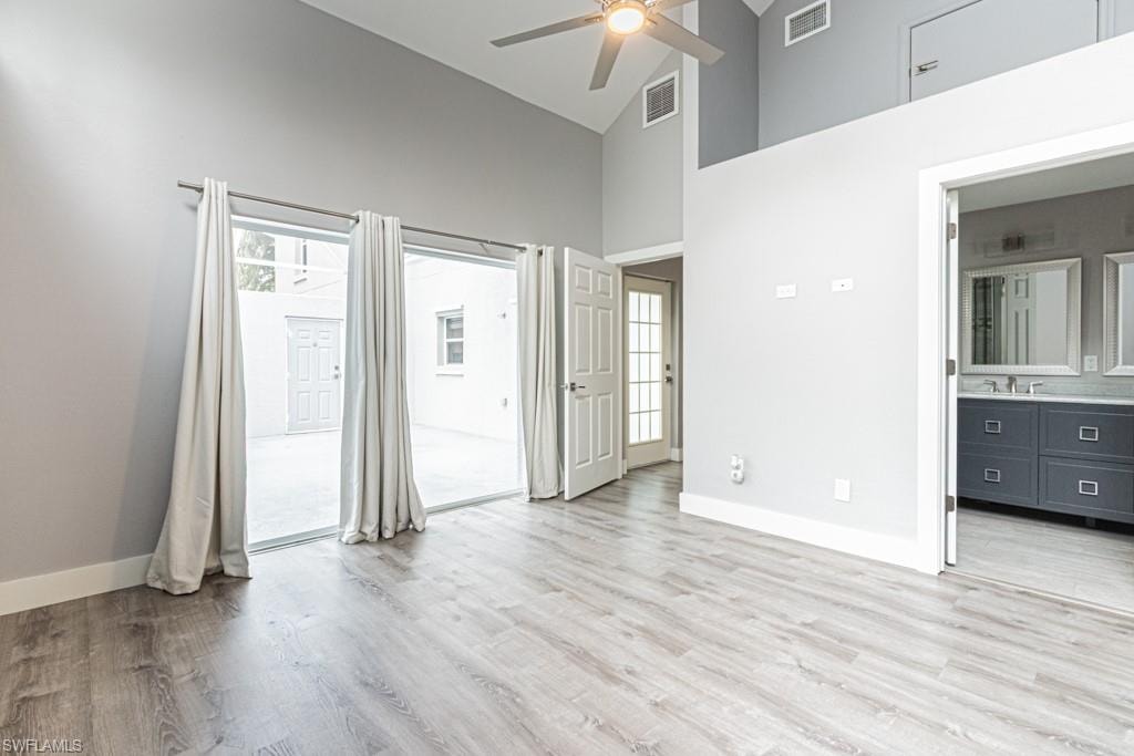Unfurnished bedroom with light wood-style floors, high vaulted ceiling, ceiling fan, and connected bathroom