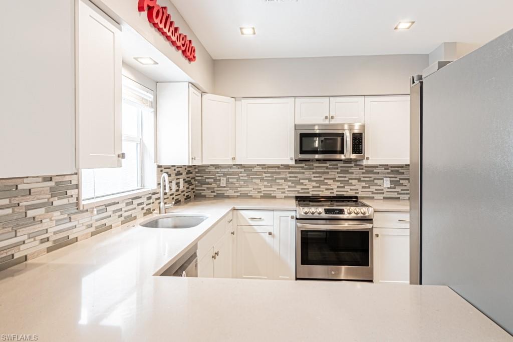 Kitchen featuring appliances with stainless steel finishes, white cabinetry, tasteful backsplash, and light stone counters