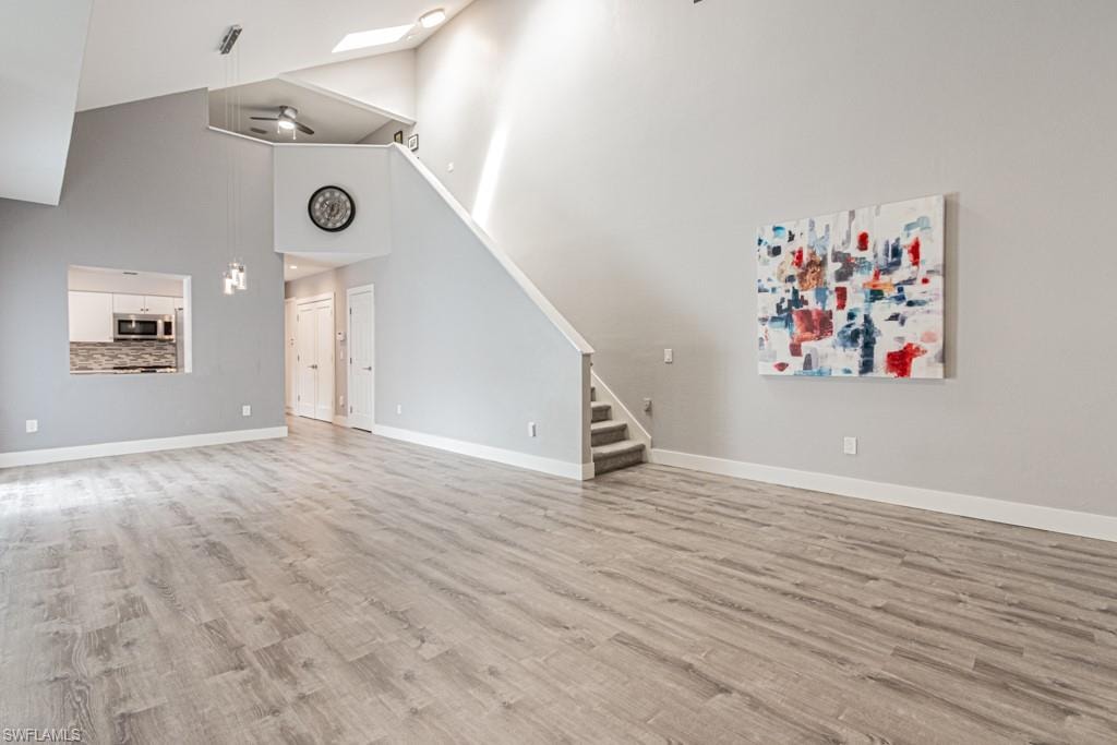 Unfurnished living room featuring light wood-style flooring, high vaulted ceiling, stairs, and a skylight