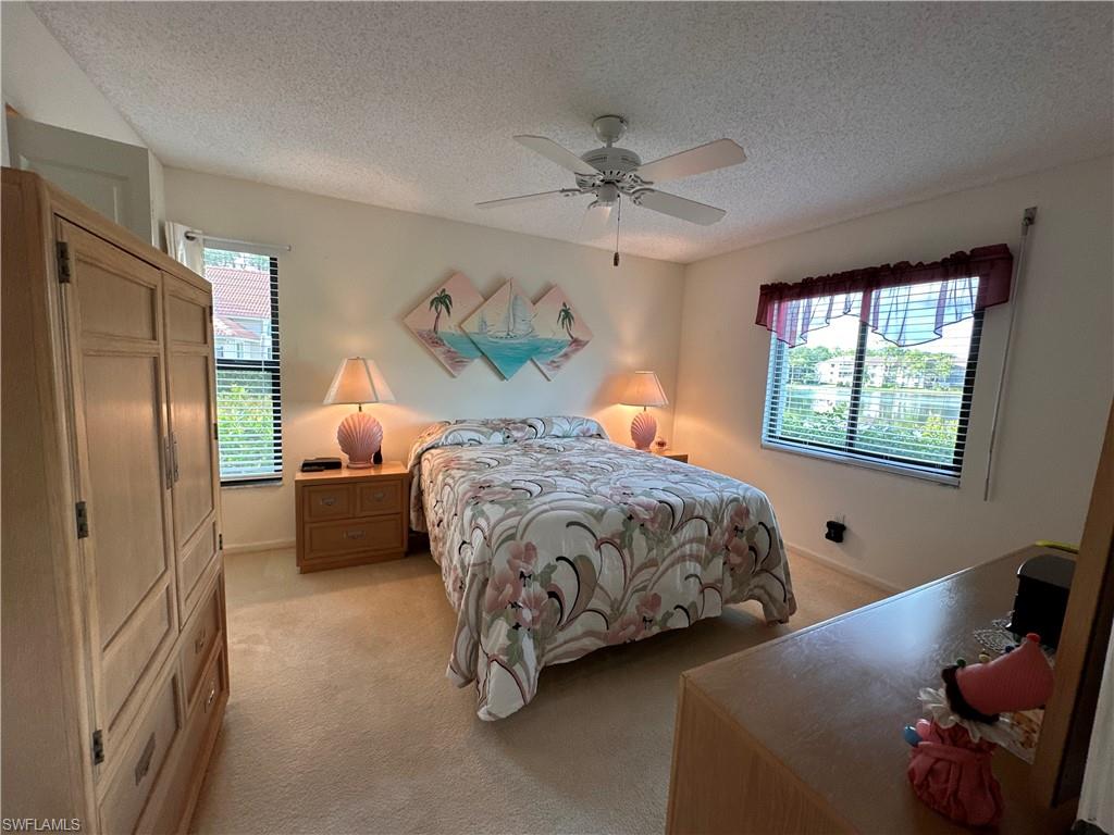 Bedroom featuring light carpet, multiple windows, a ceiling fan, impact windows and manual storm shutters