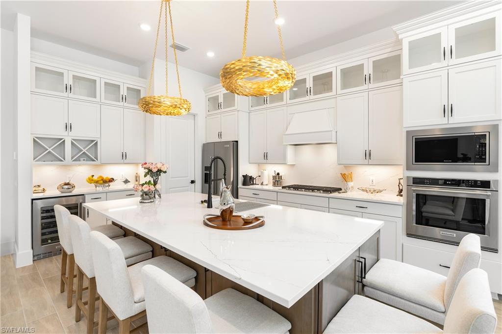 Kitchen featuring appliances with stainless steel finishes, a kitchen breakfast bar, light stone counters, recessed lighting, and wine cooler