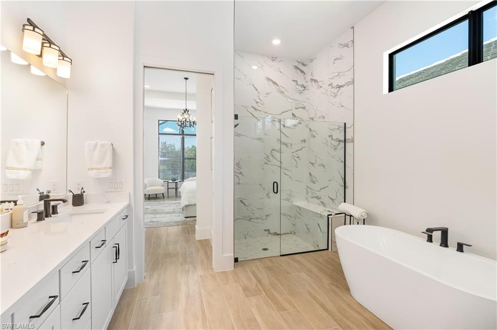 Ensuite bathroom with healthy amount of natural light, a marble finish shower, a freestanding bath, vanity, and recessed lighting