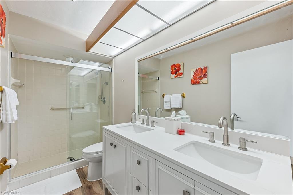 Bathroom featuring a shower stall, double vanity, and dark wood-style flooring