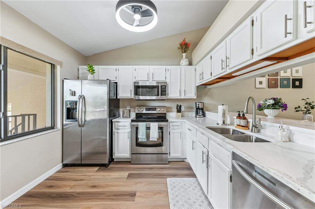 Kitchen with appliances with stainless steel finishes, light stone countertops, lofted ceiling, white cabinets, and light wood-style flooring