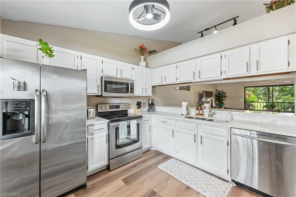 Kitchen featuring stainless steel appliances, white cabinetry, light wood finished floors, and light stone countertops