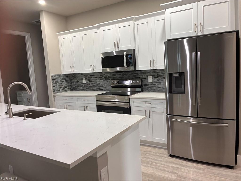 Kitchen featuring appliances with stainless steel finishes, tasteful backsplash, white cabinetry, and light stone countertops