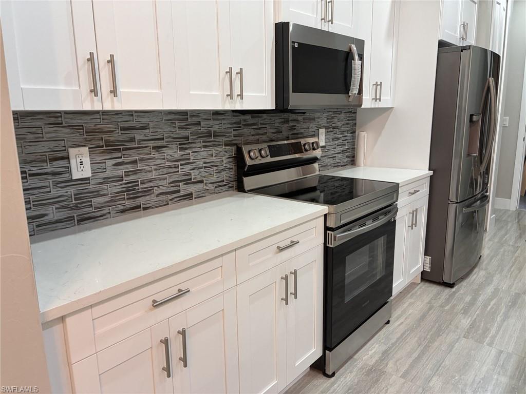Kitchen featuring appliances with stainless steel finishes, white cabinetry, tasteful backsplash, light stone countertops, and light wood-style porcelain flooring