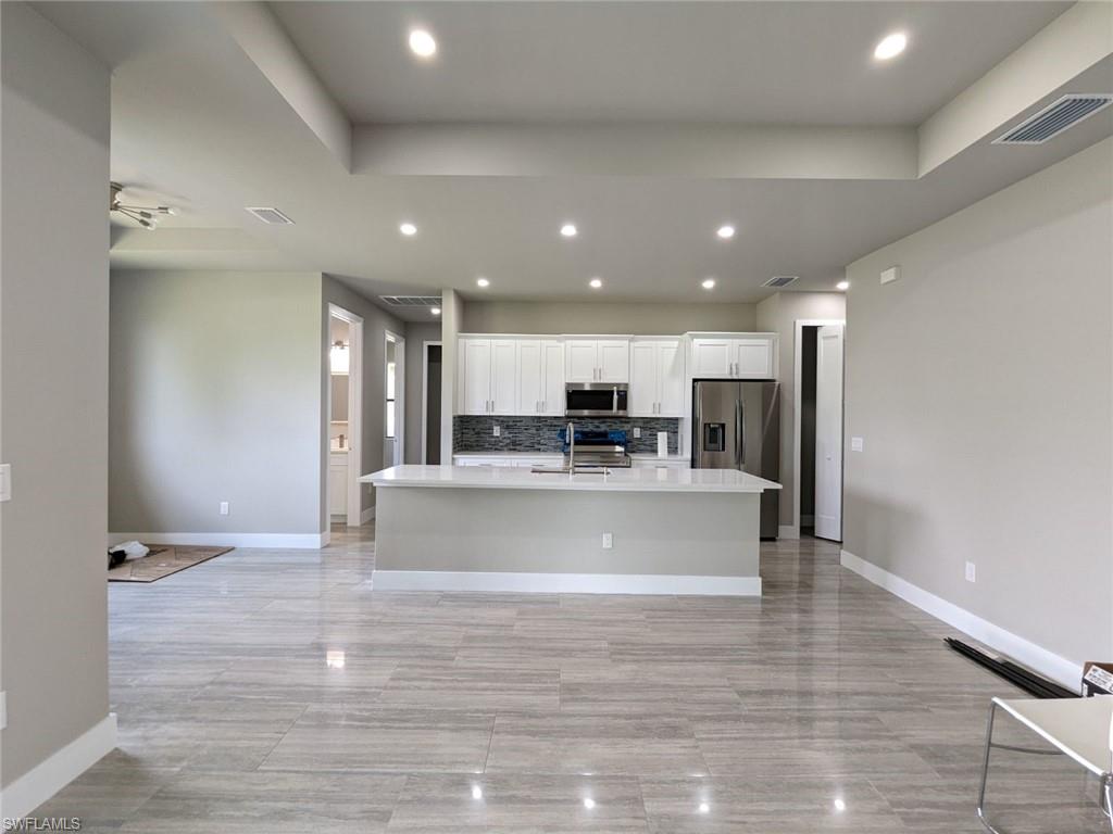 Kitchen featuring decorative backsplash, a center island with sink, white cabinetry, recessed lighting, and appliances with stainless steel finishes