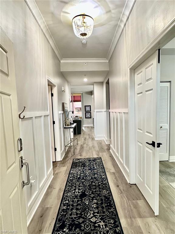 Hall featuring crown molding, light wood-type flooring, a decorative wall, and wainscoting
