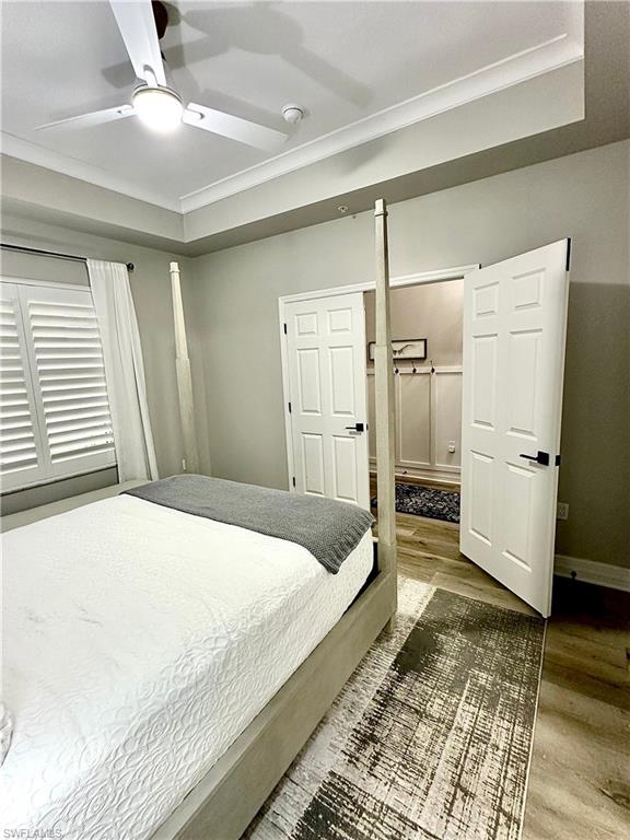 Bedroom featuring wood finished floors, a tray ceiling, ceiling fan, and crown molding