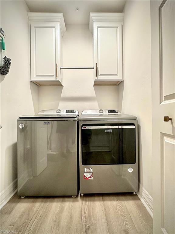 Laundry area featuring washer and dryer, light wood-type flooring, and cabinet space