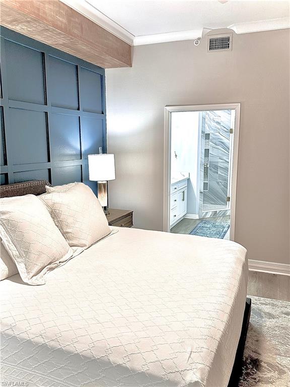 Bedroom with crown molding, light wood finished floors, and connected bathroom