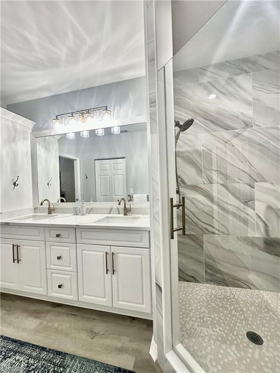 Full bathroom featuring a marble finish shower, double vanity, and light wood-style floors