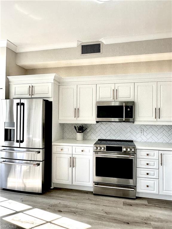Kitchen with stainless steel appliances, white cabinets, backsplash, and light stone countertops