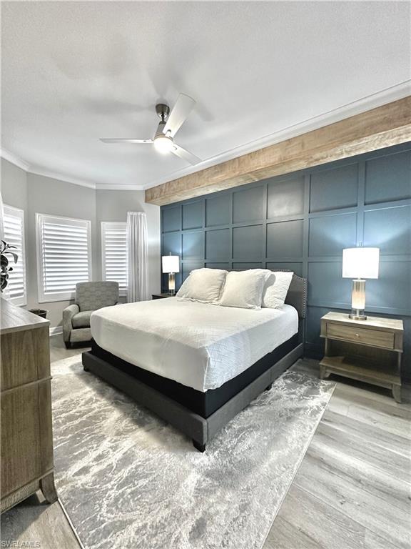 Bedroom with ornamental molding, a ceiling fan, a textured ceiling, a decorative wall, and light wood-style floors