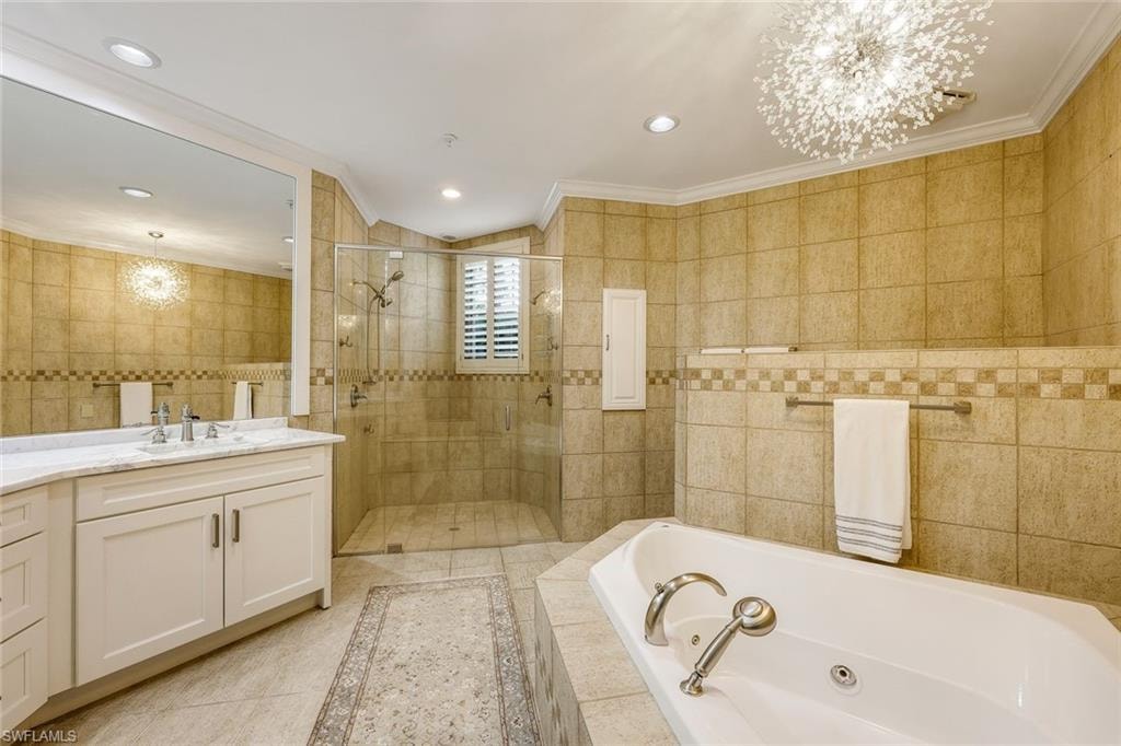 Full bath with a chandelier, vanity, a shower stall, a whirlpool tub, and tile walls