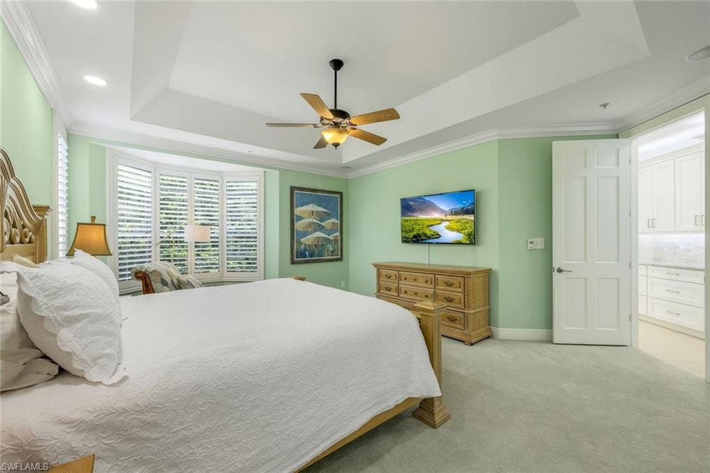 Bedroom with a raised ceiling, ornamental molding, light carpet, ceiling fan, and recessed lighting