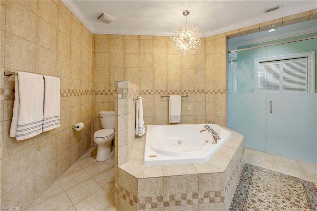Full bathroom with a stall shower, tile walls, a jetted tub, a chandelier, and crown molding
