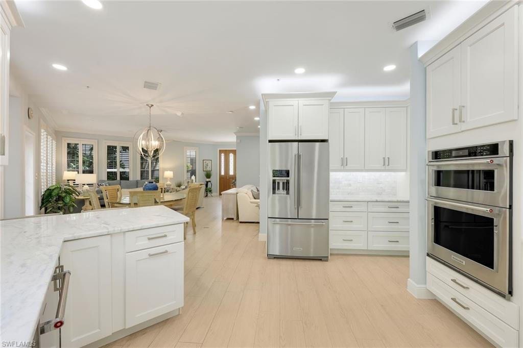 Kitchen featuring appliances with stainless steel finishes, white cabinets, light stone countertops, open floor plan, and light wood finished floors