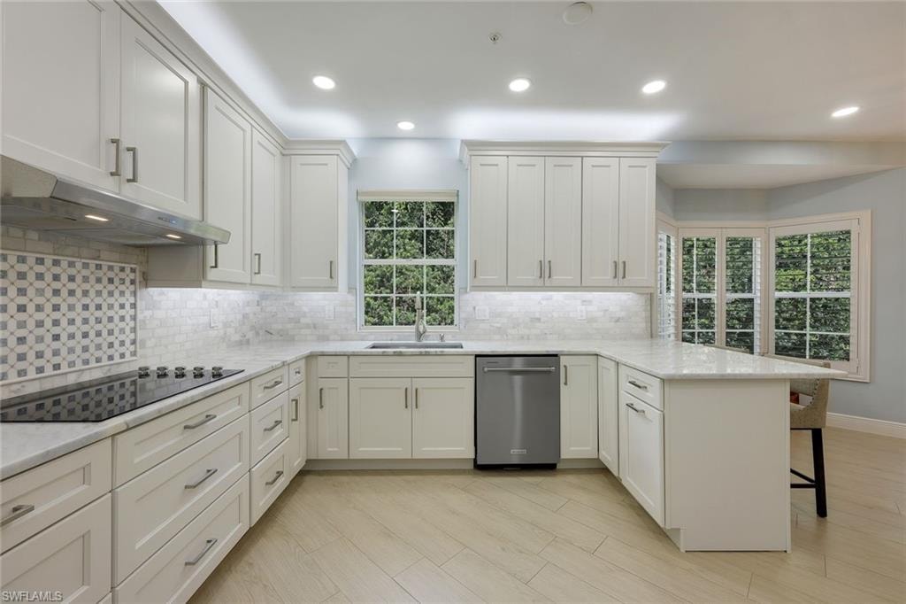 Kitchen with a peninsula, decorative backsplash, recessed lighting, dishwasher, and light stone counters
