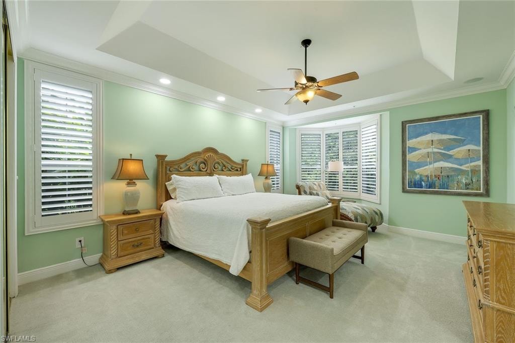 Bedroom with a tray ceiling, ornamental molding, light colored carpet, a ceiling fan, and recessed lighting