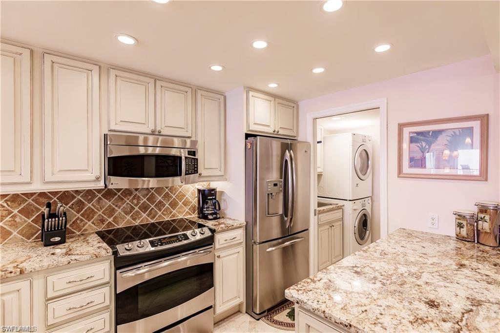 Kitchen featuring appliances with stainless steel finishes, estacked washer and dryer, recessed lighting, light stone countertops, and backsplash