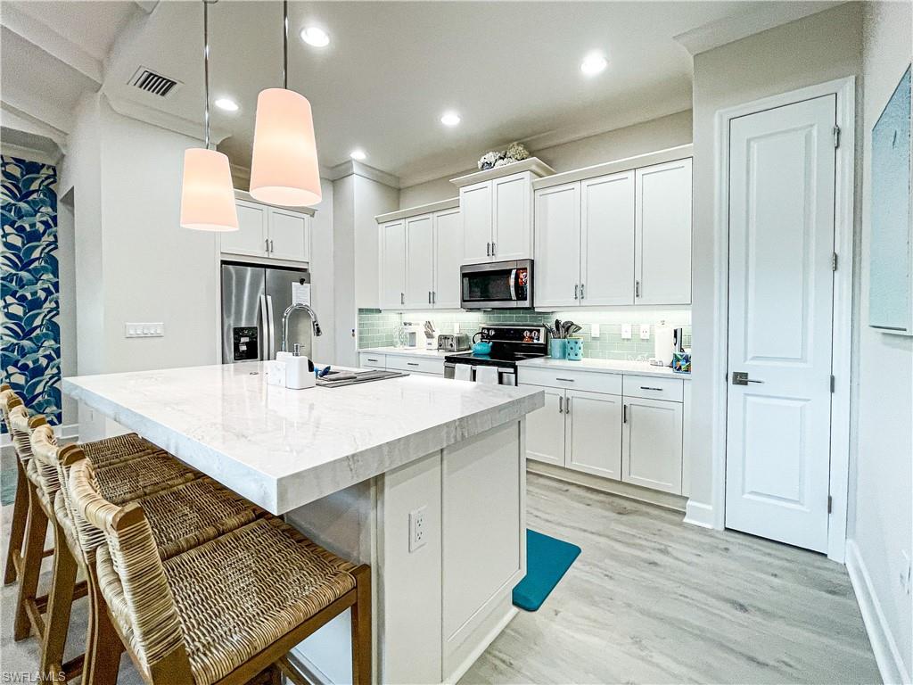 Kitchen with decorative light fixtures, a center island with sink, light hardwood / wood-style floors, stainless steel appliances, and white cabinets