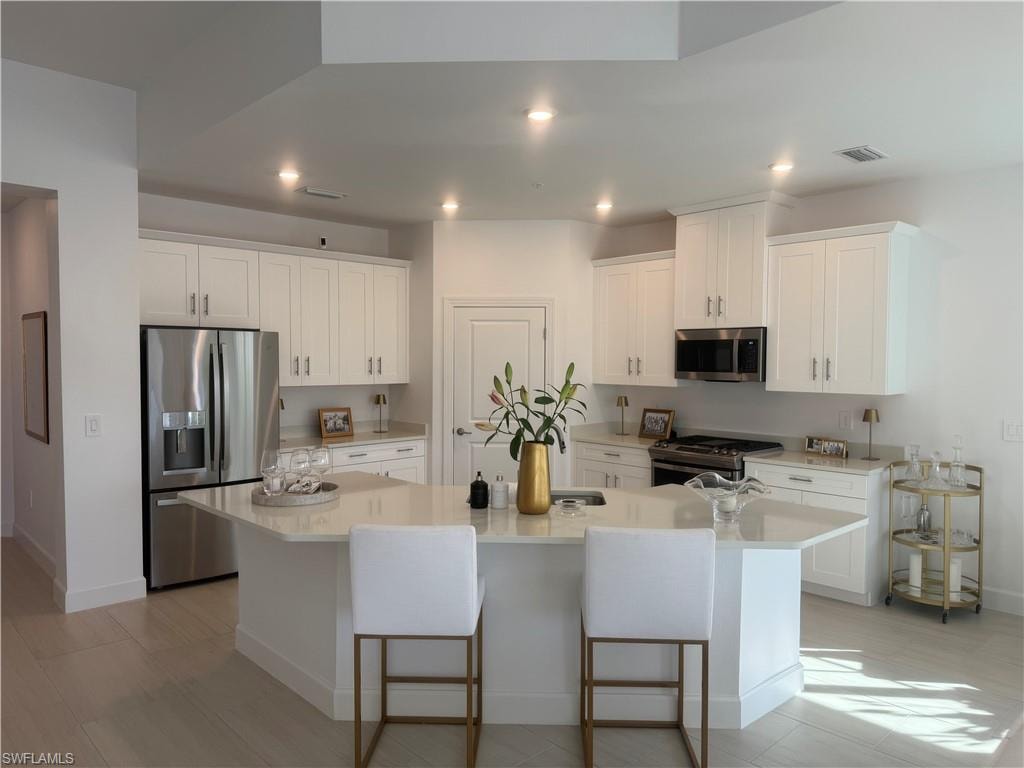 Kitchen with stainless steel appliances, white cabinets, a kitchen bar, an island with sink, and light stone countertops