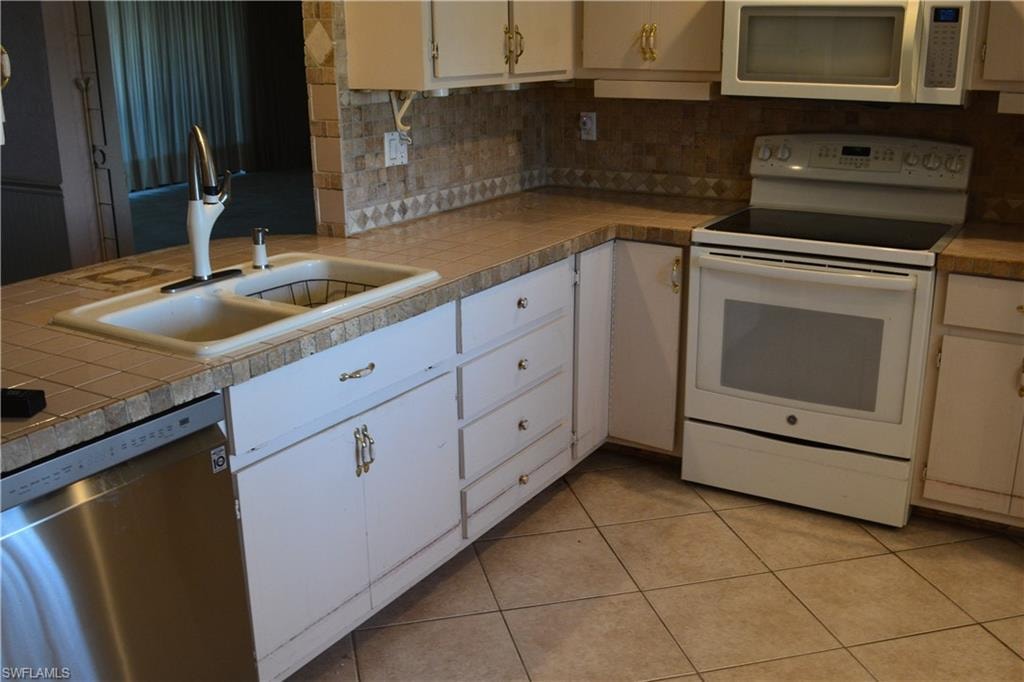 Kitchen featuring white range with electric stovetop, tasteful backsplash, stainless steel dishwasher, and tile countertops