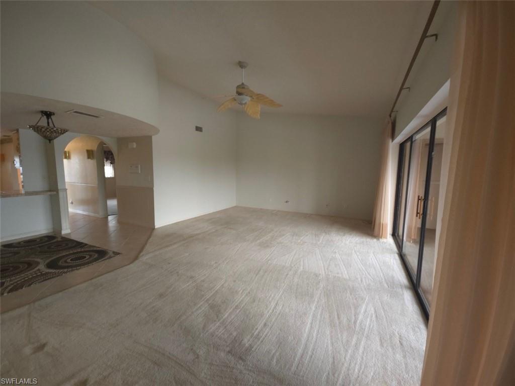 Unfurnished living room featuring arched walkways, light tile patterned flooring, ceiling fan, and light colored carpet