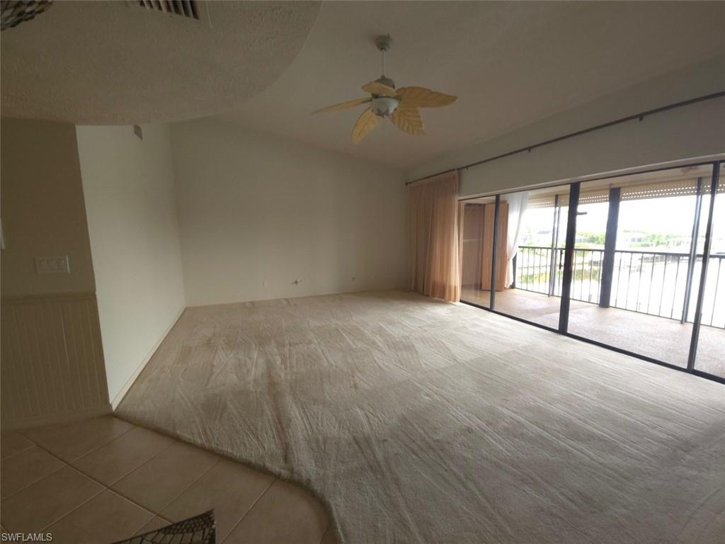 Carpeted empty room featuring tile patterned floors, a wainscoted wall, and ceiling fan