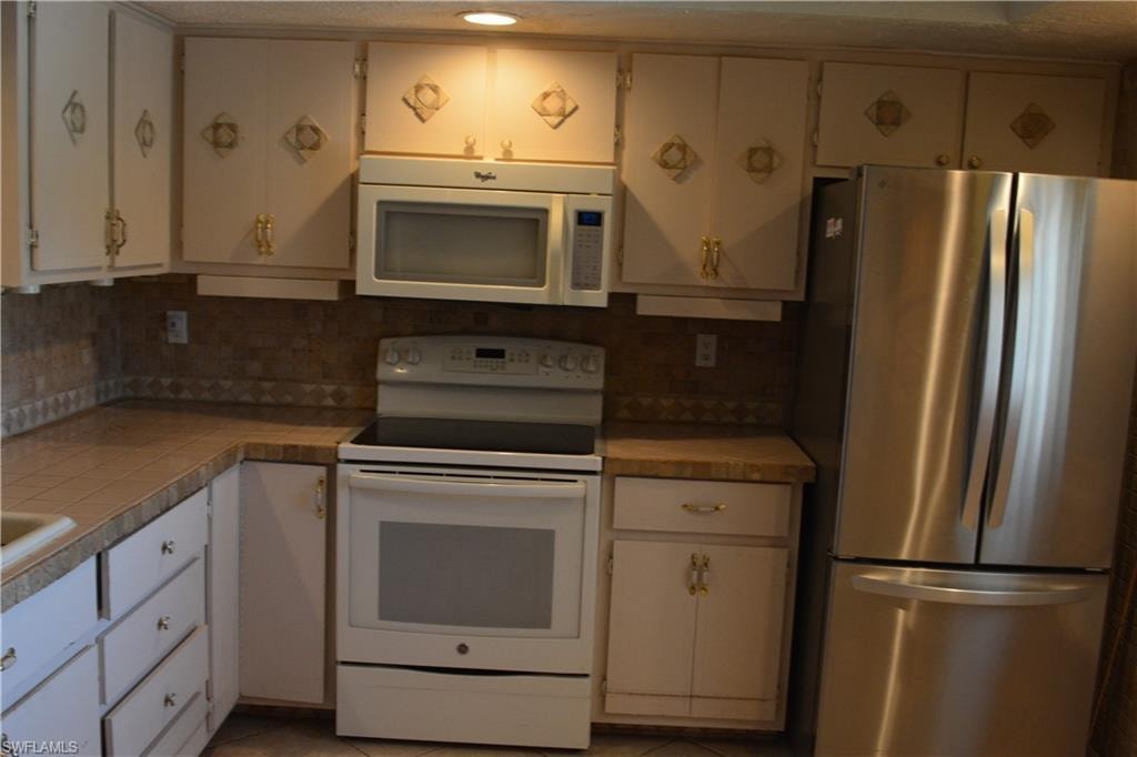 Kitchen featuring white appliances, backsplash, white cabinetry, and a textured ceiling