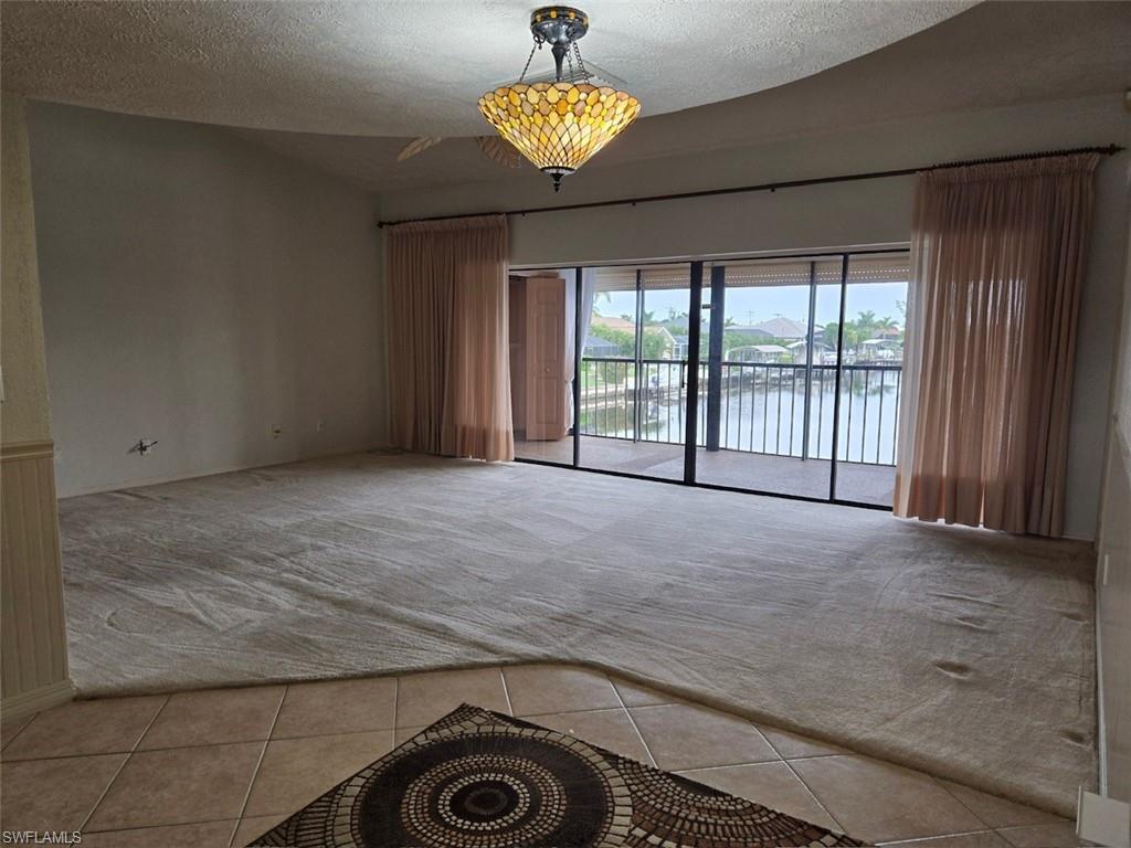 Living room with textured ceiling, a water view, tile patterned flooring, and vaulted ceiling