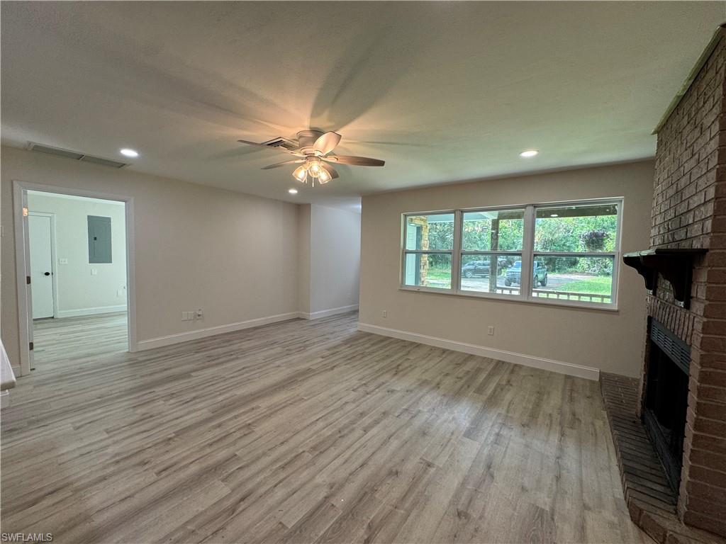 Unfurnished living room featuring light wood-type flooring, a brick fireplace, recessed lighting, ceiling fan, and electric panel