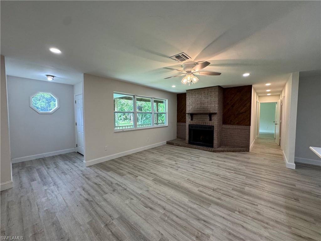 Unfurnished living room featuring ceiling fan, light wood finished floors, recessed lighting, and a brick fireplace