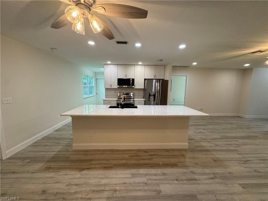 Kitchen with a ceiling fan, stainless steel appliances, light wood finished floors, recessed lighting, and a center island with sink