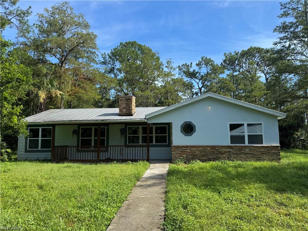 View of front facade with stone siding, stucco siding, a metal roof, a front lawn, and covered porch